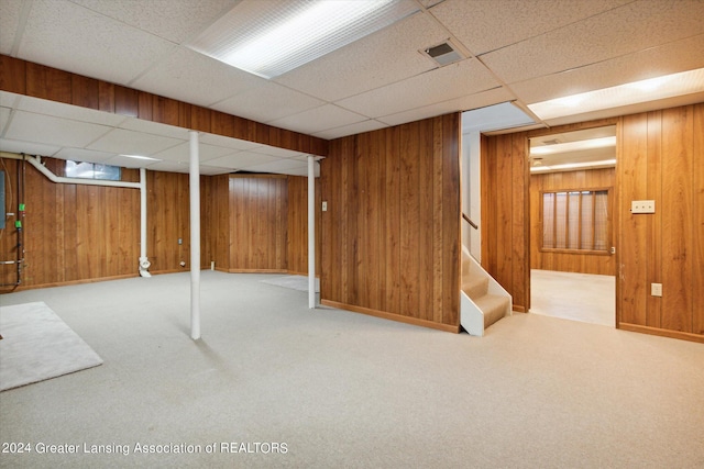 basement featuring light carpet, wood walls, and a paneled ceiling