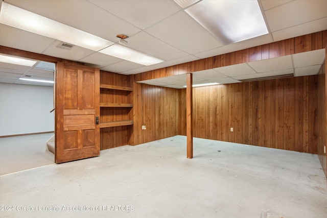 basement featuring a drop ceiling and wooden walls