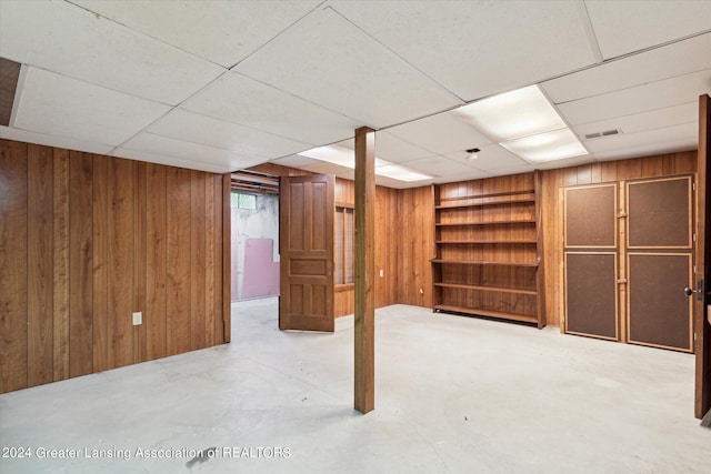 basement featuring a paneled ceiling and wood walls