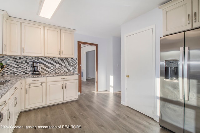 kitchen featuring light stone counters, stainless steel fridge, cream cabinetry, light wood-type flooring, and decorative backsplash