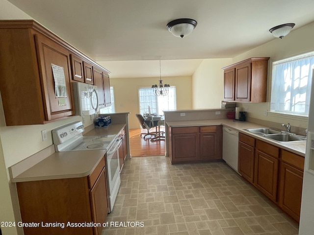 kitchen with white appliances, sink, kitchen peninsula, hanging light fixtures, and a chandelier