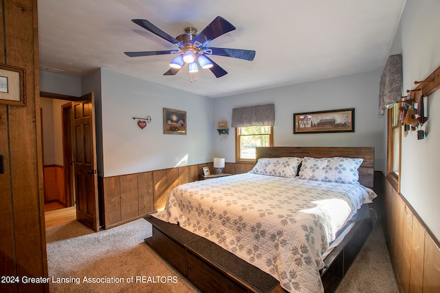 bedroom with light colored carpet, ceiling fan, and wooden walls