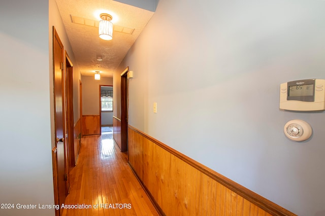 hall with a textured ceiling, light hardwood / wood-style floors, and wooden walls