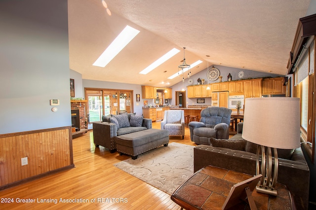 living room featuring a textured ceiling, light wood-type flooring, lofted ceiling with skylight, and wood walls