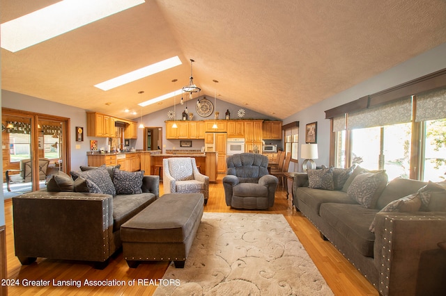 living room with vaulted ceiling with skylight, light hardwood / wood-style floors, and a textured ceiling