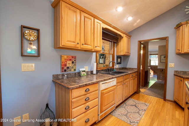 kitchen featuring paneled dishwasher, sink, vaulted ceiling, dark stone countertops, and light hardwood / wood-style floors