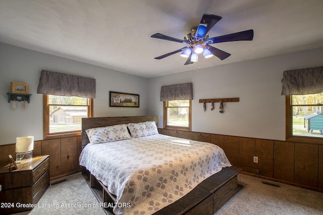 carpeted bedroom with ceiling fan and wood walls