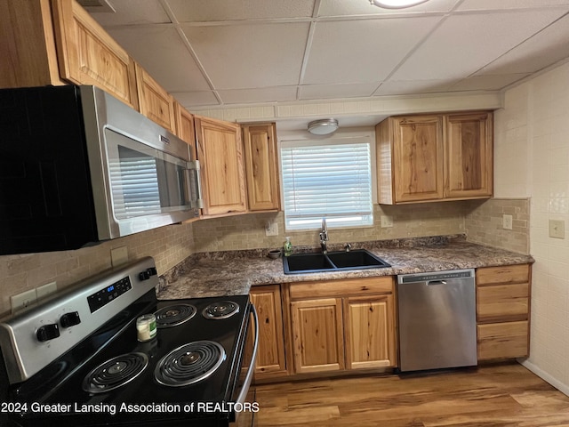 kitchen with light wood-type flooring, a paneled ceiling, sink, stainless steel appliances, and backsplash