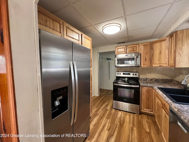 kitchen featuring sink, tasteful backsplash, a paneled ceiling, stainless steel appliances, and light wood-type flooring