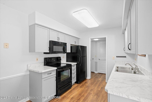 kitchen with light wood-type flooring, black appliances, sink, and light stone countertops