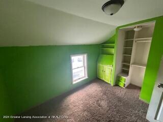 unfurnished bedroom featuring lofted ceiling, a closet, and dark colored carpet