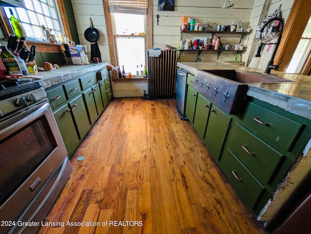 kitchen with green cabinets, wooden walls, stainless steel range, and light hardwood / wood-style flooring