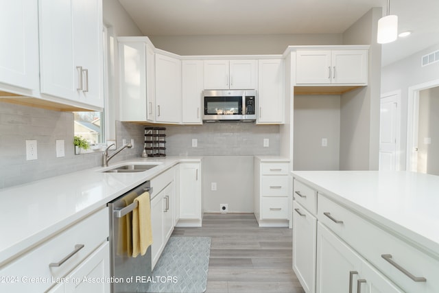 kitchen with stainless steel appliances, a sink, light countertops, and decorative light fixtures