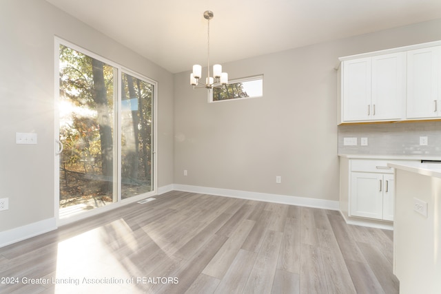 unfurnished dining area featuring light wood finished floors, baseboards, and an inviting chandelier