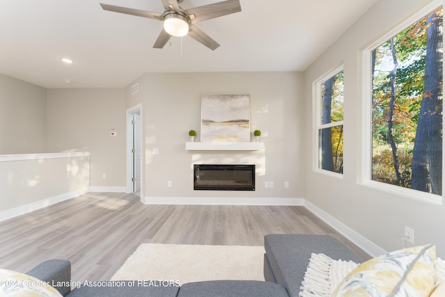 living area featuring light wood-style floors, visible vents, baseboards, and a glass covered fireplace