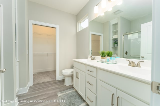 full bathroom featuring wood finished floors, a shower with shower door, a sink, and double vanity