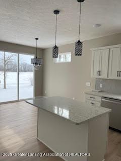 kitchen featuring white cabinets, a center island, decorative light fixtures, light stone countertops, and stainless steel dishwasher