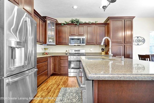 kitchen with light stone counters, an island with sink, sink, light hardwood / wood-style flooring, and appliances with stainless steel finishes