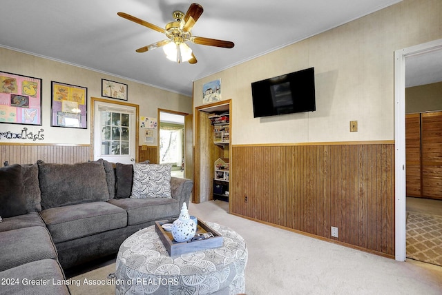 living room with crown molding, ceiling fan, wood walls, and light colored carpet