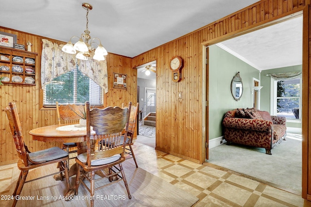 dining room with ceiling fan with notable chandelier, crown molding, wood walls, and a healthy amount of sunlight