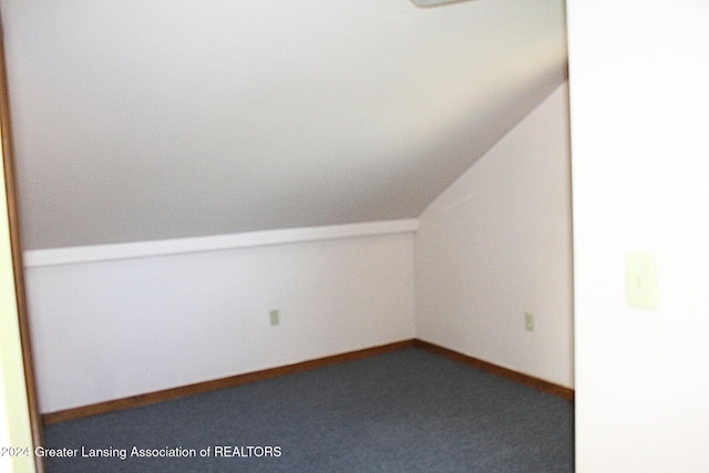 additional living space with dark colored carpet and vaulted ceiling