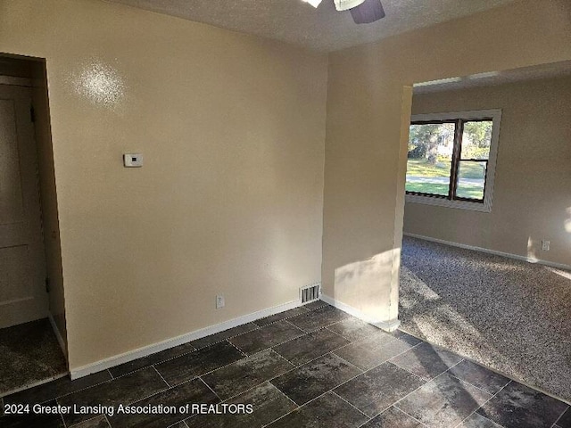 unfurnished room with ceiling fan, dark carpet, and a textured ceiling