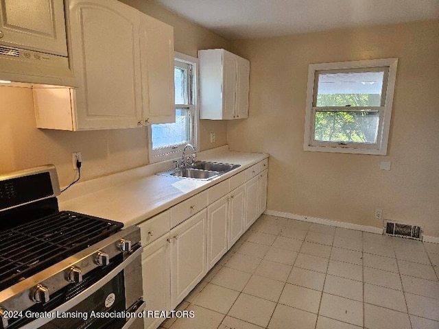 kitchen with gas range, sink, light tile patterned floors, and white cabinetry