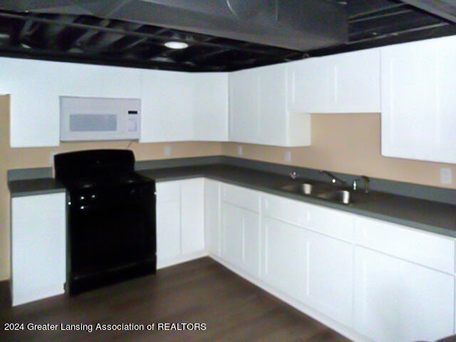 kitchen with black range, white cabinets, sink, and dark hardwood / wood-style flooring