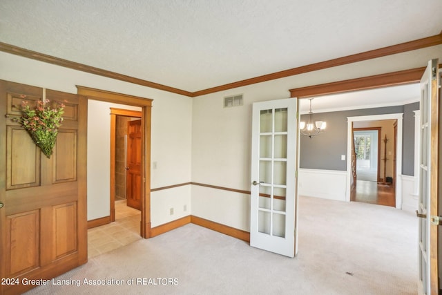 carpeted spare room with ornamental molding, french doors, a chandelier, and a textured ceiling