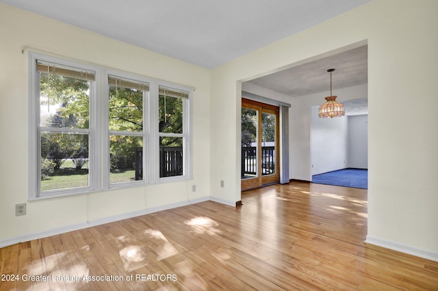 spare room with a notable chandelier, wood-type flooring, and a healthy amount of sunlight