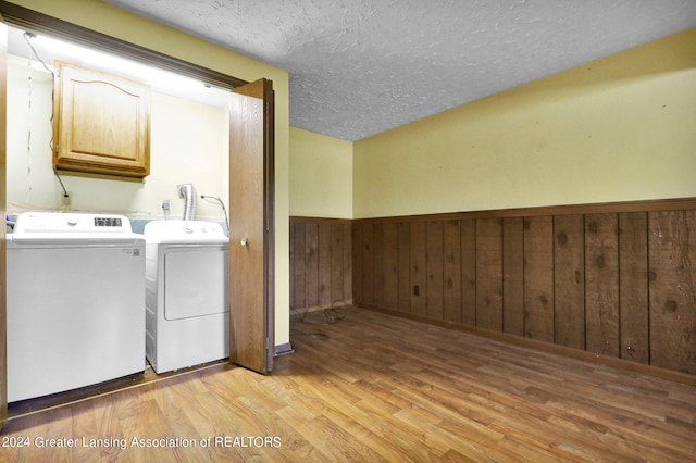 laundry room with wooden walls, washing machine and clothes dryer, cabinets, a textured ceiling, and light hardwood / wood-style floors