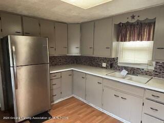 kitchen with light hardwood / wood-style floors, tasteful backsplash, sink, and stainless steel fridge