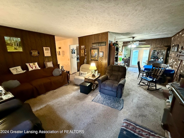 carpeted living room with french doors, ceiling fan, a textured ceiling, and wood walls