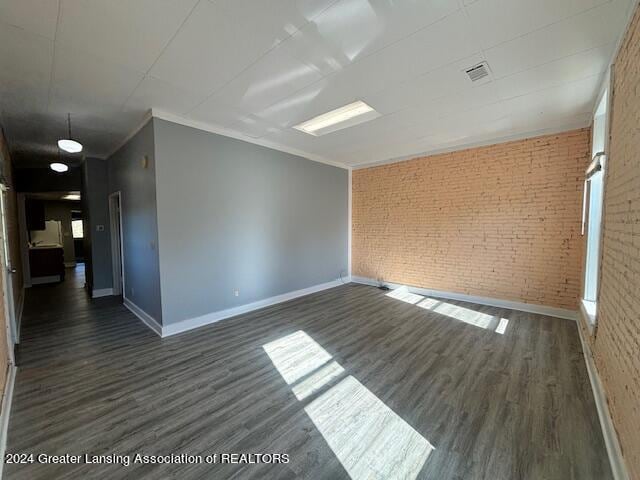 spare room featuring brick wall, crown molding, and dark hardwood / wood-style flooring