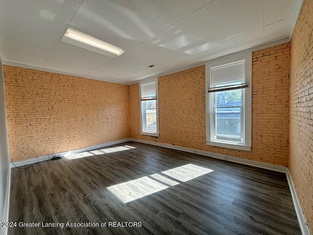 unfurnished room with dark hardwood / wood-style floors and brick wall