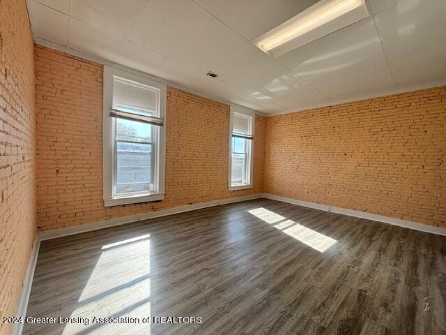 spare room featuring brick wall, dark hardwood / wood-style flooring, and plenty of natural light