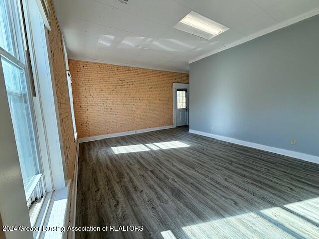 unfurnished room featuring brick wall, dark wood-type flooring, and ornamental molding