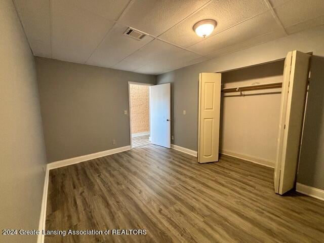 unfurnished bedroom with a closet, a paneled ceiling, and dark hardwood / wood-style floors