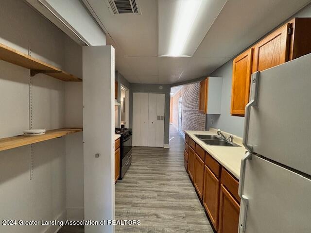 kitchen featuring stainless steel refrigerator, black range, light hardwood / wood-style floors, sink, and brick wall