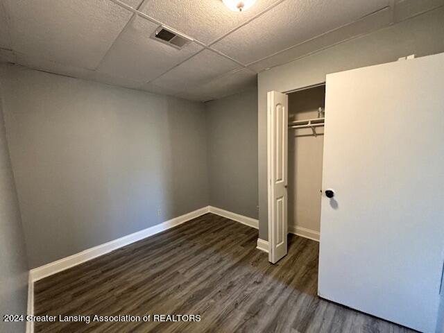 unfurnished bedroom featuring a drop ceiling, a closet, and dark hardwood / wood-style flooring