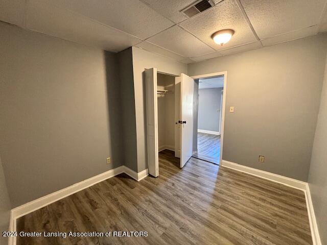 unfurnished bedroom featuring a closet, a paneled ceiling, and dark wood-type flooring