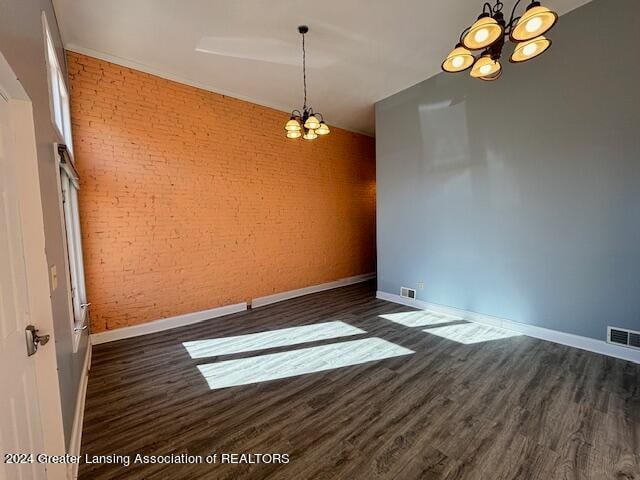 empty room with brick wall, an inviting chandelier, and dark hardwood / wood-style flooring