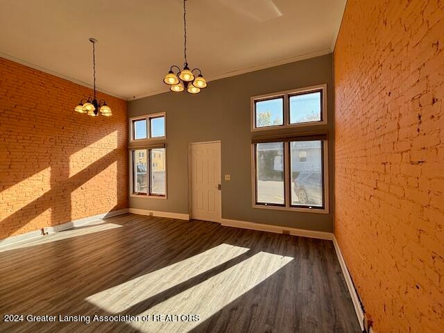 interior space featuring a notable chandelier, dark wood-type flooring, brick wall, and crown molding