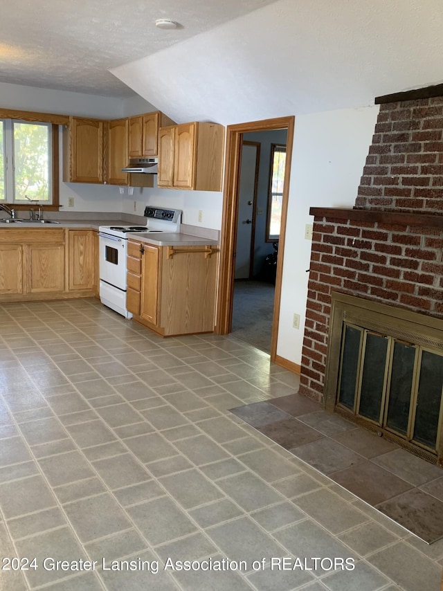 kitchen featuring sink, electric range, vaulted ceiling, a textured ceiling, and a fireplace