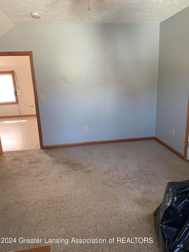 carpeted empty room with vaulted ceiling and a textured ceiling