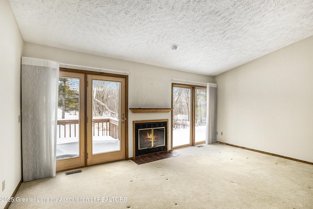 unfurnished living room featuring carpet floors, a fireplace with flush hearth, visible vents, and baseboards