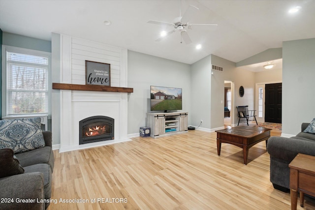 living room featuring vaulted ceiling, a fireplace, light hardwood / wood-style floors, and ceiling fan