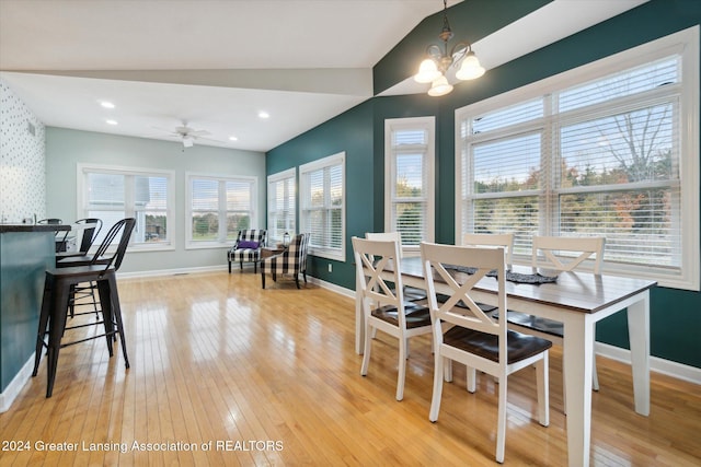 dining room with light hardwood / wood-style floors, a healthy amount of sunlight, ceiling fan with notable chandelier, and vaulted ceiling