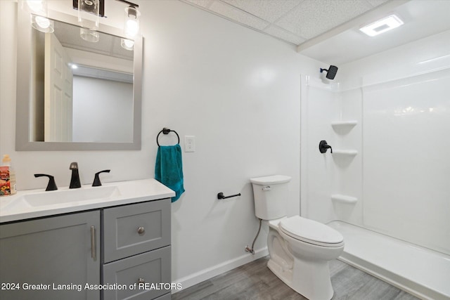 bathroom with hardwood / wood-style flooring, toilet, a shower, vanity, and a paneled ceiling