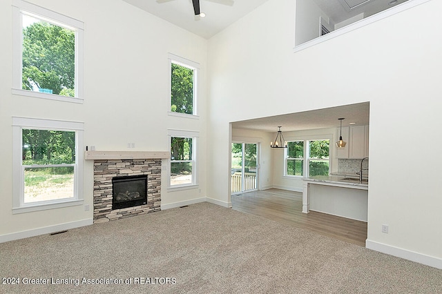 unfurnished living room with ceiling fan with notable chandelier, carpet floors, a stone fireplace, and high vaulted ceiling